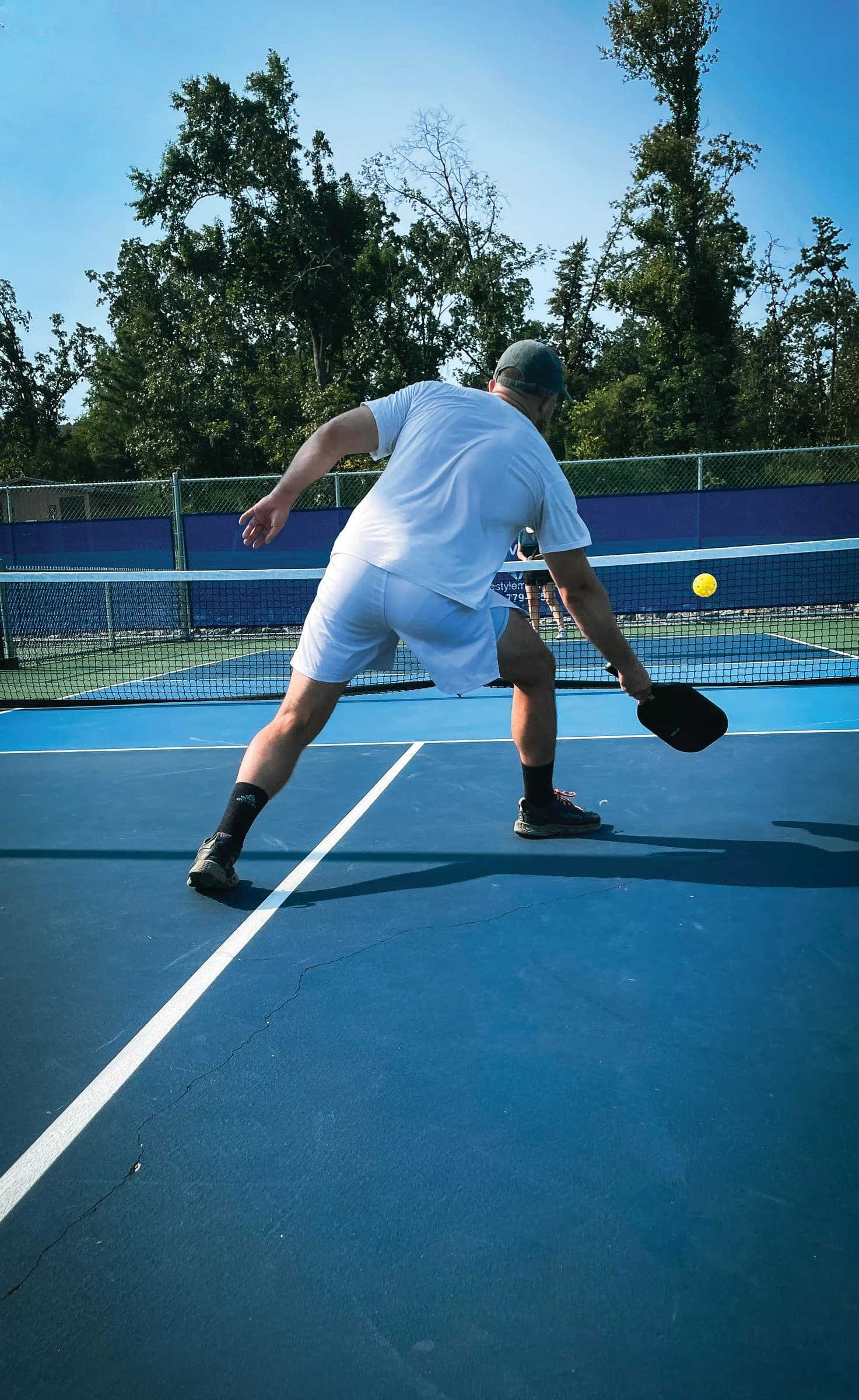 A player reaching for a pickleball on a blue outdoor court