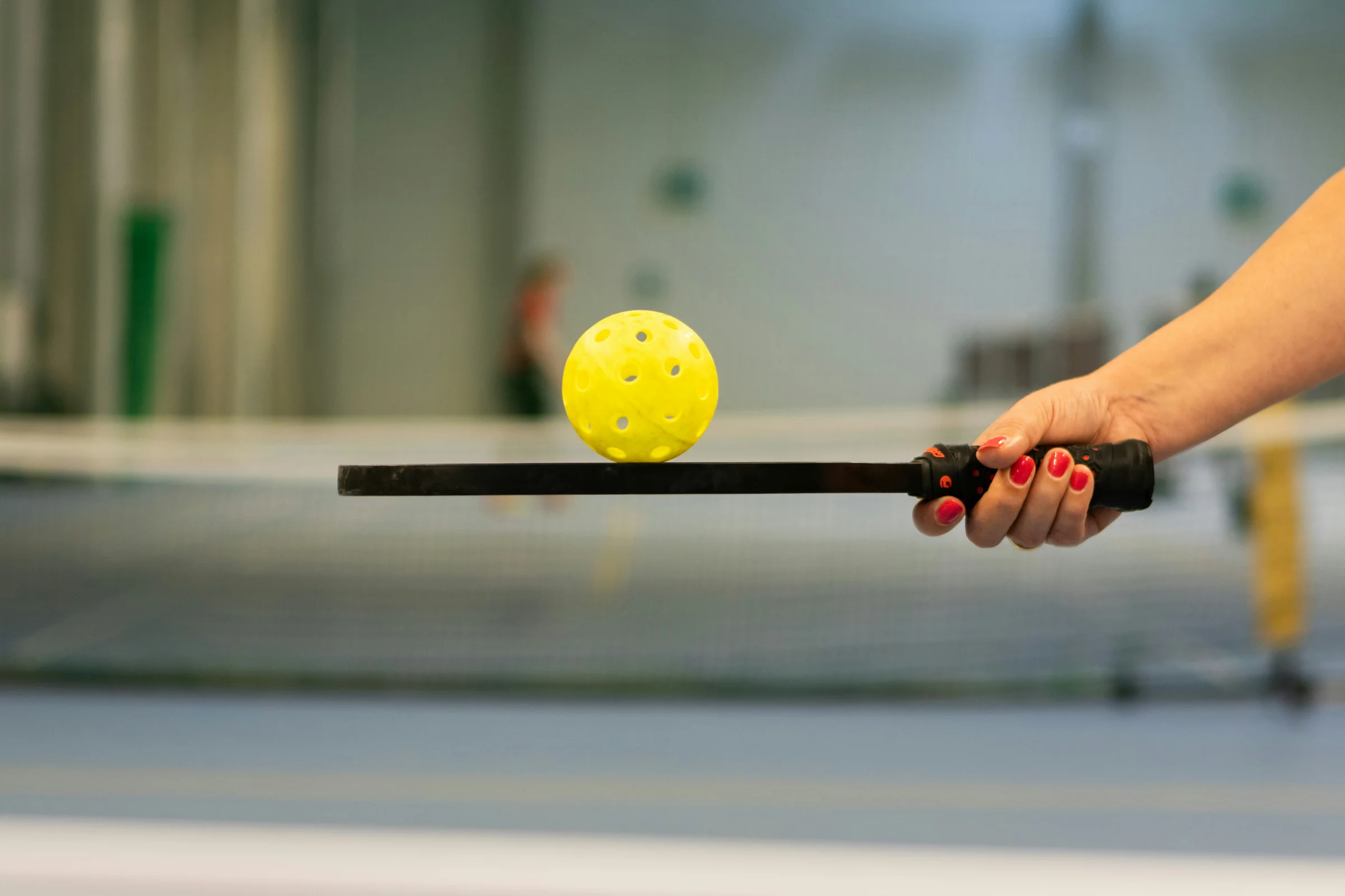 A yellow pickleball balanced on the edge of a paddle